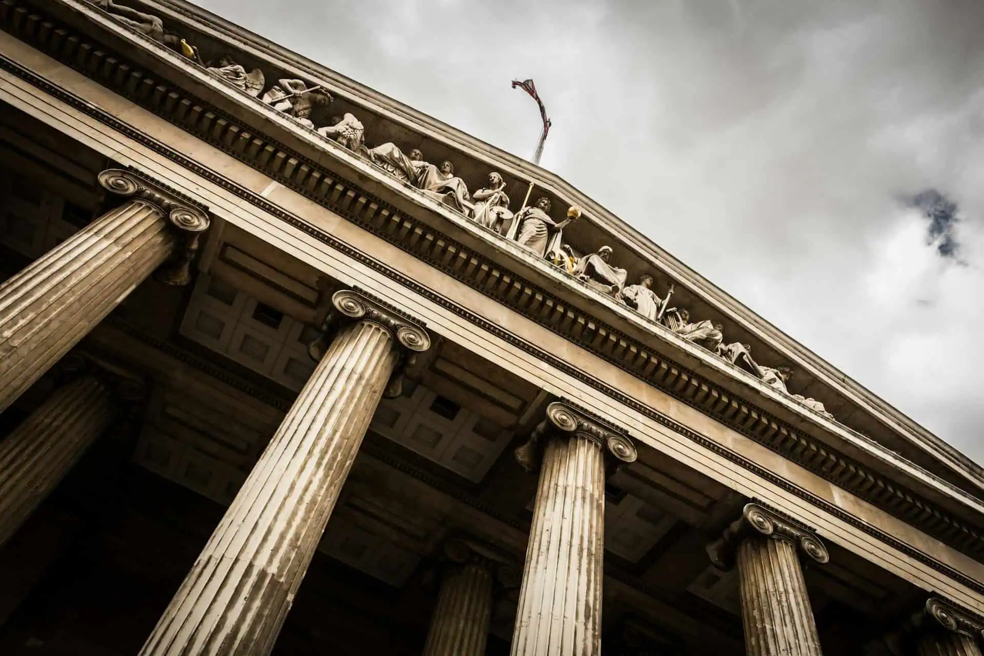 Façade néoclassique avec colonnes et sculptures, ciel nuageux